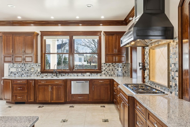 kitchen with light stone counters, a sink, wall chimney range hood, stainless steel gas stovetop, and backsplash