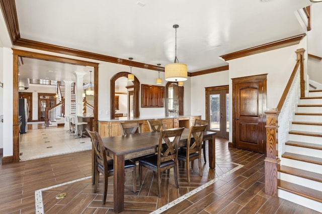 dining space with arched walkways, wood finish floors, baseboards, ornamental molding, and stairway