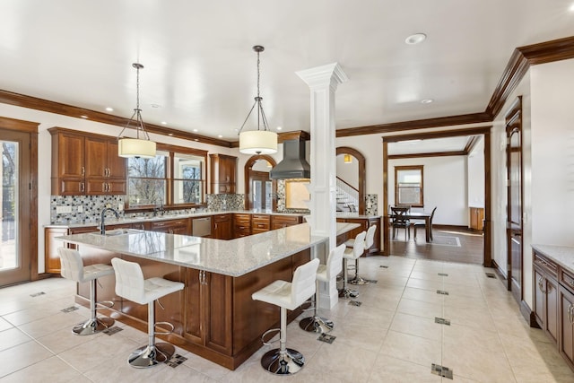 kitchen with light tile patterned floors, wall chimney range hood, brown cabinetry, and a breakfast bar area