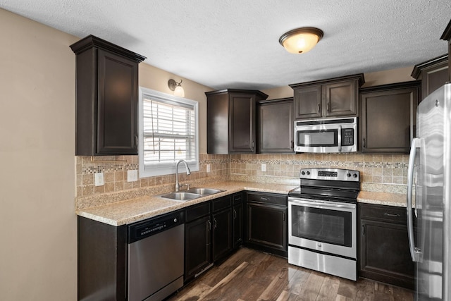 kitchen with stainless steel appliances, a sink, light countertops, backsplash, and dark wood finished floors