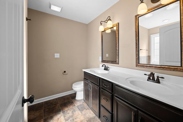 bathroom featuring double vanity, baseboards, toilet, and a sink