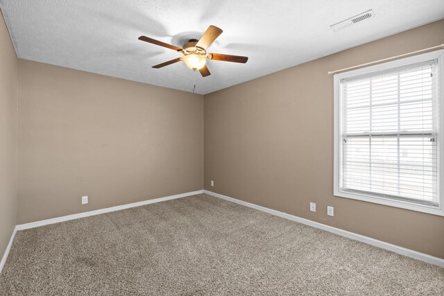 empty room featuring a textured ceiling, carpet floors, a ceiling fan, visible vents, and baseboards