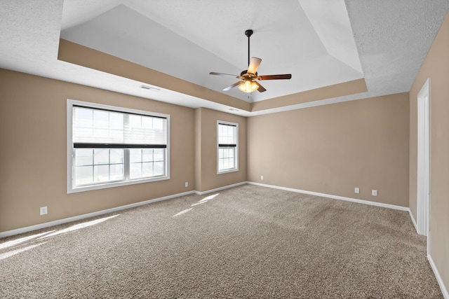 empty room featuring a tray ceiling, visible vents, and baseboards