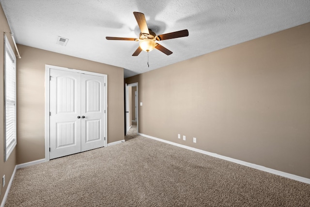 unfurnished bedroom featuring baseboards, visible vents, a textured ceiling, carpet floors, and a closet