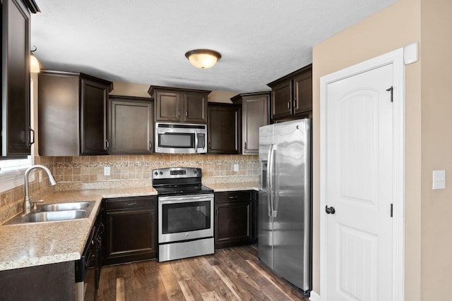 kitchen with a sink, dark brown cabinets, appliances with stainless steel finishes, decorative backsplash, and dark wood finished floors