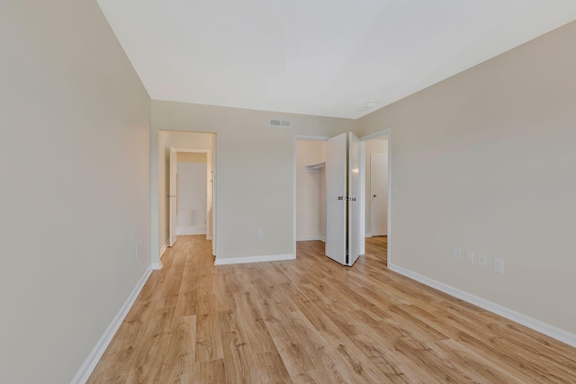 unfurnished bedroom with a walk in closet, light wood finished floors, a closet, visible vents, and baseboards