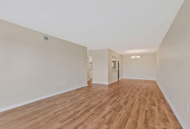 unfurnished living room with an inviting chandelier, baseboards, visible vents, and light wood finished floors