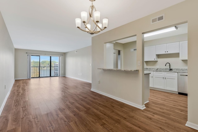 unfurnished living room with baseboards, visible vents, wood finished floors, an inviting chandelier, and a sink