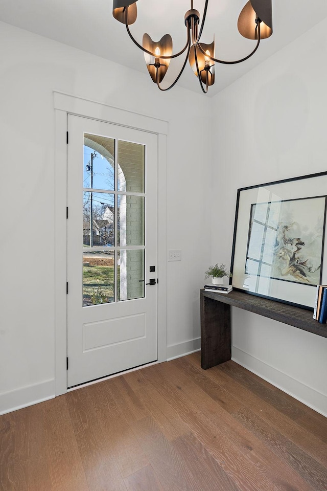 doorway with baseboards, a chandelier, and wood finished floors