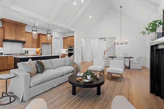 living room featuring light wood finished floors, stairway, beamed ceiling, high vaulted ceiling, and a notable chandelier