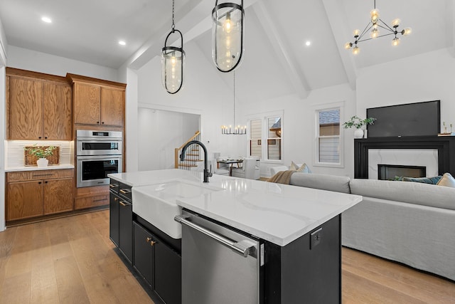 kitchen featuring appliances with stainless steel finishes, brown cabinetry, a sink, and an inviting chandelier