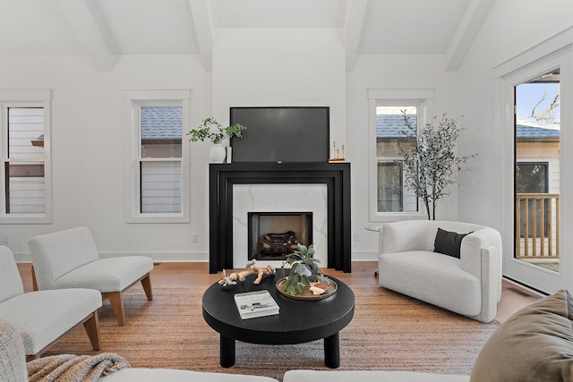 living room with a fireplace, beamed ceiling, baseboards, and wood finished floors