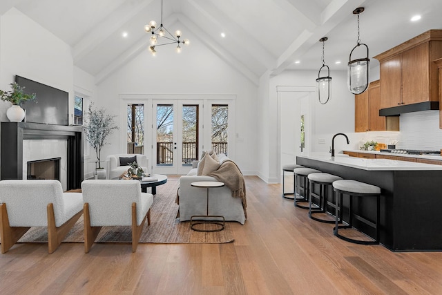 living room with french doors, light wood-style floors, high vaulted ceiling, beam ceiling, and a high end fireplace