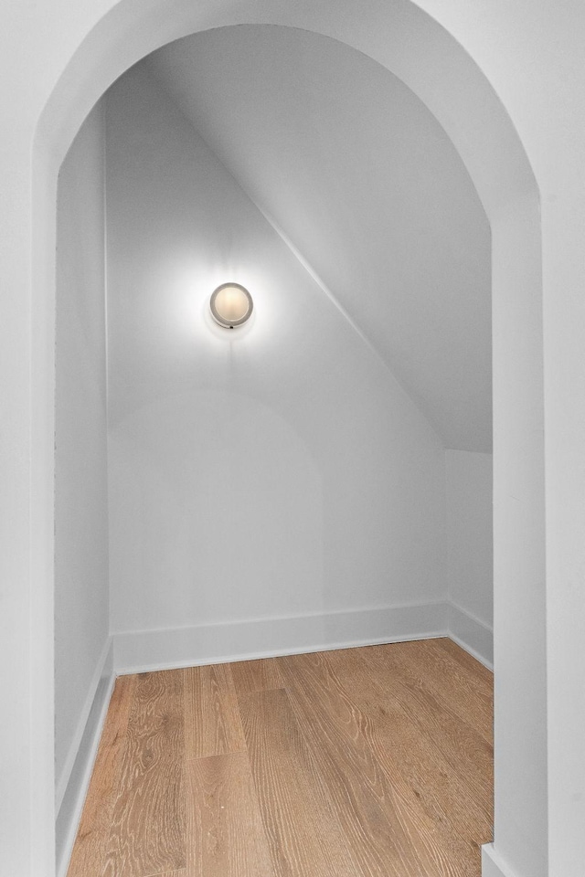 bonus room with lofted ceiling, arched walkways, light wood-style flooring, and baseboards