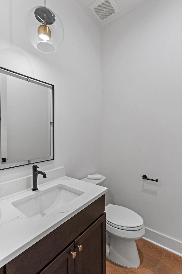 half bath featuring visible vents, toilet, vanity, wood finished floors, and baseboards