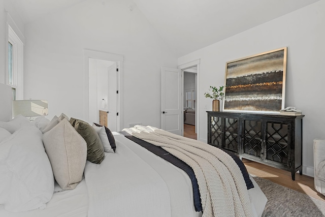 bedroom with lofted ceiling, wood finished floors, and ensuite bathroom