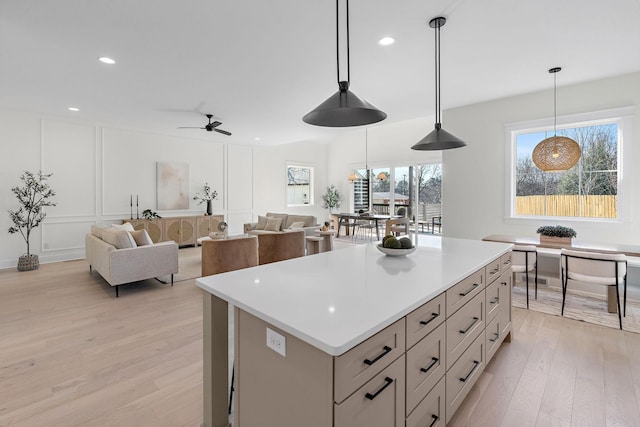 kitchen with pendant lighting, light countertops, a decorative wall, light wood-style floors, and a kitchen island