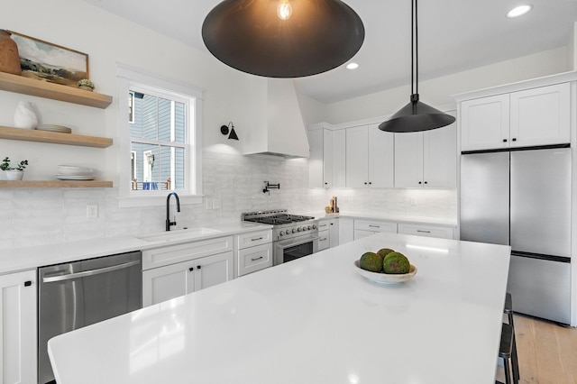 kitchen featuring light wood finished floors, stainless steel appliances, premium range hood, white cabinetry, and a sink