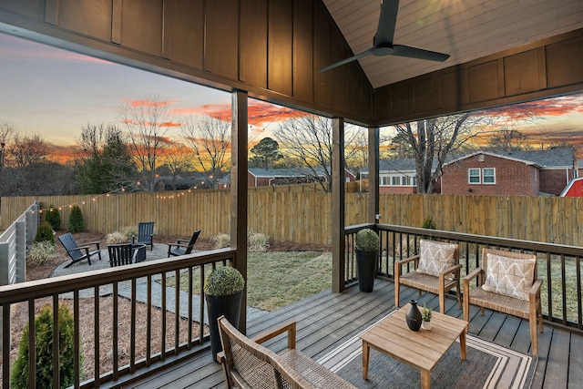 deck at dusk with a fenced backyard, a fire pit, and a ceiling fan