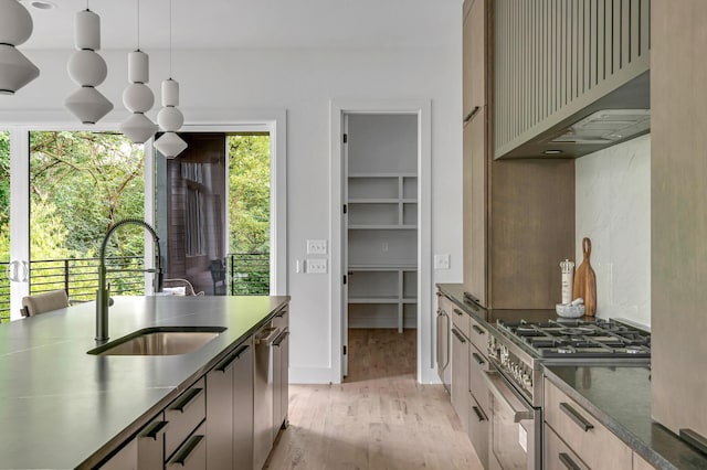 kitchen featuring custom exhaust hood, stainless steel appliances, hanging light fixtures, light wood-style flooring, and a sink