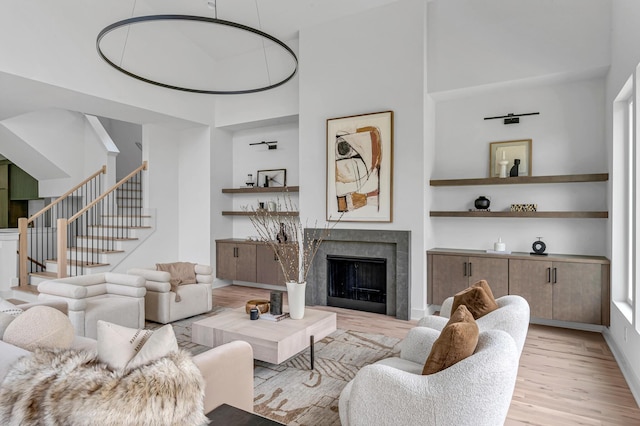 living room featuring a towering ceiling, a high end fireplace, wood finished floors, baseboards, and stairs