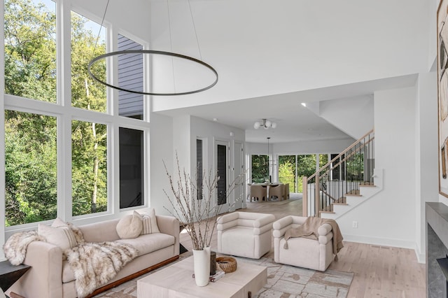 living area with light wood-style flooring, a high ceiling, stairway, and baseboards