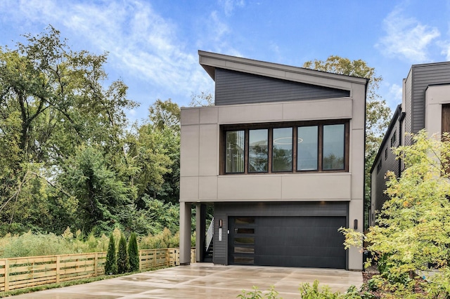 contemporary house with a garage, concrete driveway, fence, and stucco siding