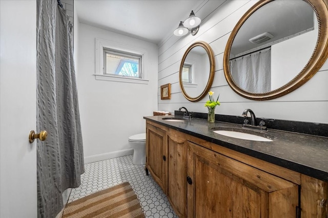 bathroom featuring double vanity, toilet, baseboards, and a sink