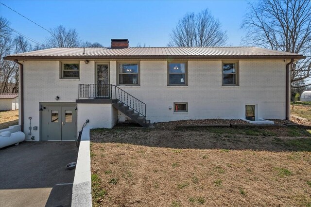 view of front of home with a front yard, metal roof, brick siding, and a chimney