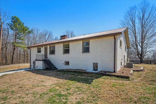 back of house featuring fence, a chimney, central air condition unit, brick siding, and metal roof