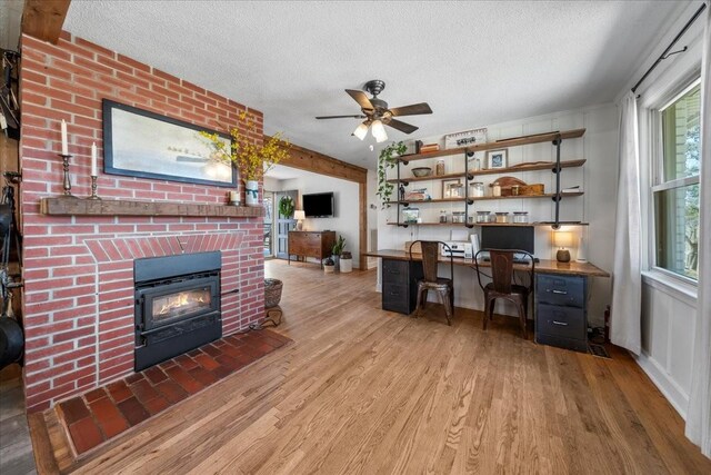 office space featuring ceiling fan, a fireplace, wood finished floors, a textured ceiling, and built in study area