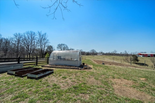 view of yard with a rural view, an outdoor structure, a greenhouse, and fence