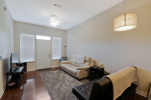 living area with ceiling fan, concrete floors, visible vents, and baseboards