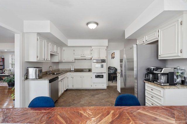 kitchen featuring light stone counters, under cabinet range hood, stainless steel appliances, a sink, and white cabinetry