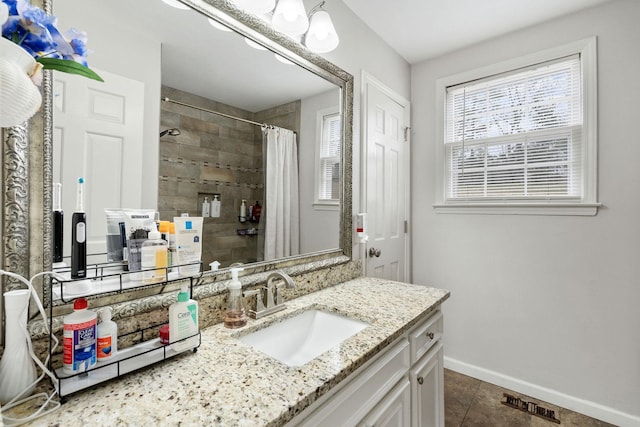 bathroom with vanity, a tile shower, a wealth of natural light, and baseboards