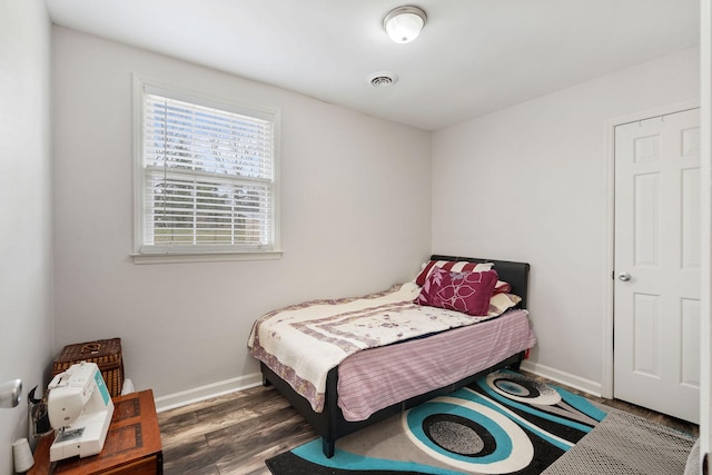 bedroom with baseboards, visible vents, and wood finished floors