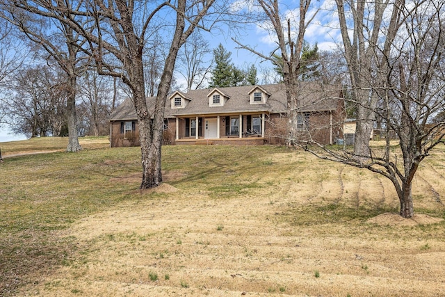 cape cod house with a porch, brick siding, a front lawn, and roof with shingles