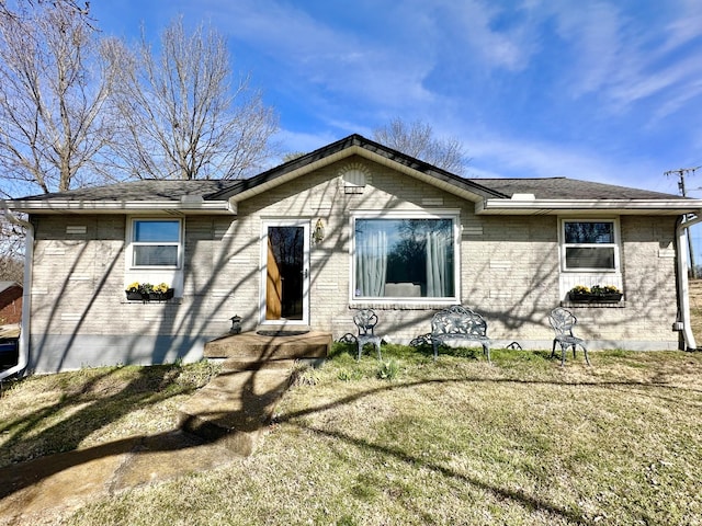 rear view of property featuring a yard, brick siding, and a shingled roof