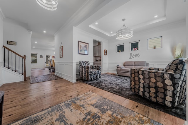 living area with a tray ceiling, a notable chandelier, hardwood / wood-style floors, and stairs