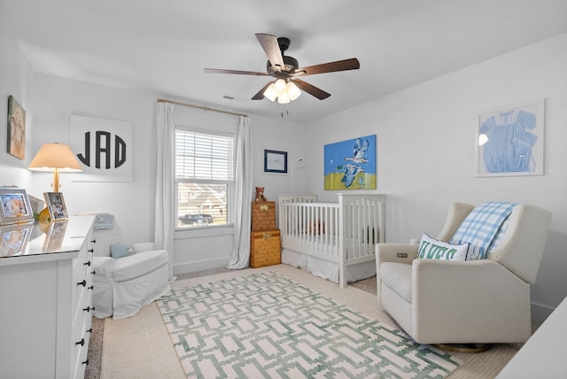 bedroom featuring light colored carpet, visible vents, baseboards, a ceiling fan, and a nursery area