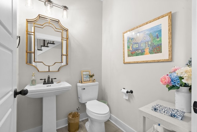 half bath featuring baseboards, a sink, toilet, and tile patterned floors