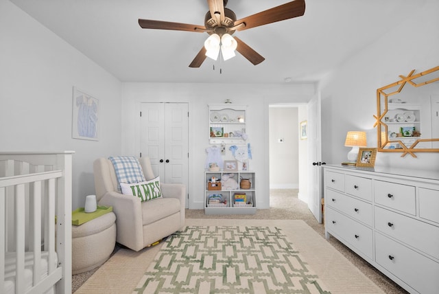 bedroom featuring a closet, light colored carpet, a ceiling fan, a crib, and baseboards