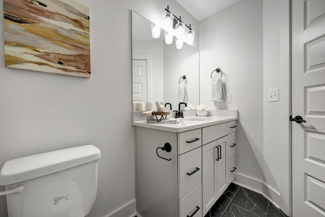 bathroom with marble finish floor, vanity, toilet, and baseboards