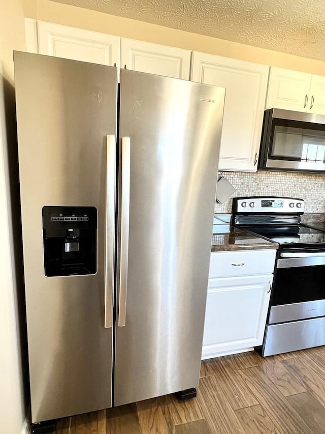 kitchen featuring stainless steel appliances, dark countertops, white cabinets, and backsplash