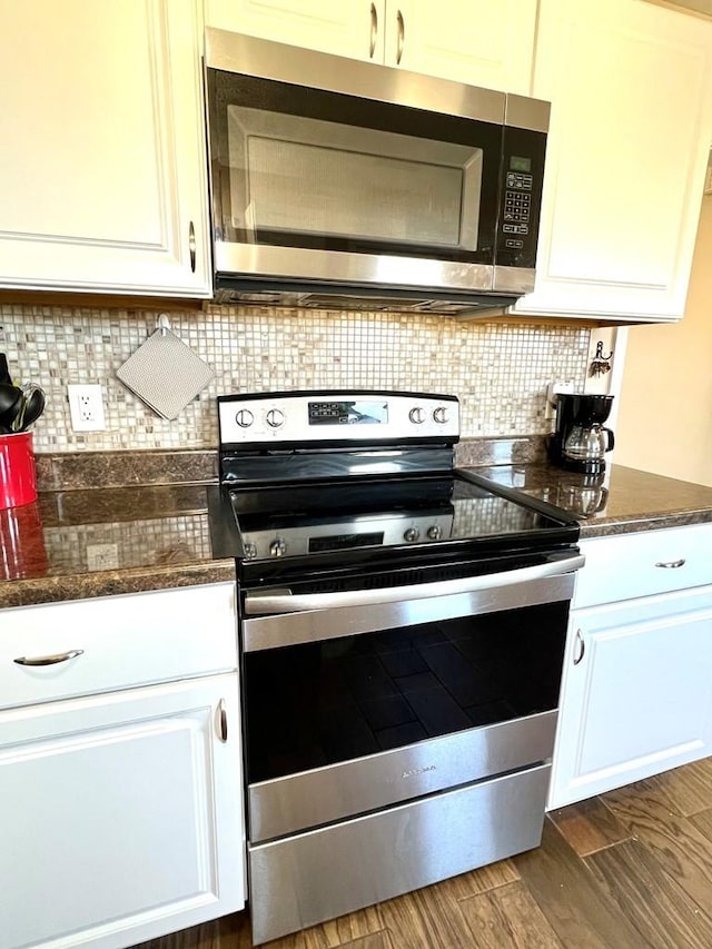 kitchen with decorative backsplash, appliances with stainless steel finishes, dark wood-type flooring, white cabinetry, and dark stone counters