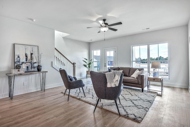 living area featuring a ceiling fan, wood finished floors, baseboards, and stairs