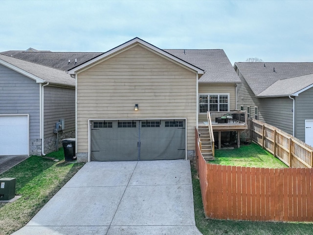 view of front facade featuring a shingled roof, concrete driveway, stairway, fence, and a front yard