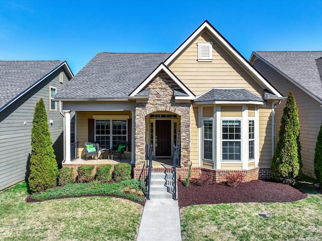 view of front facade with stone siding, a shingled roof, and a front yard