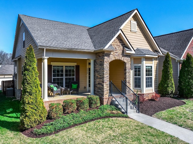 view of front of house featuring stone siding, a shingled roof, a front lawn, and a porch