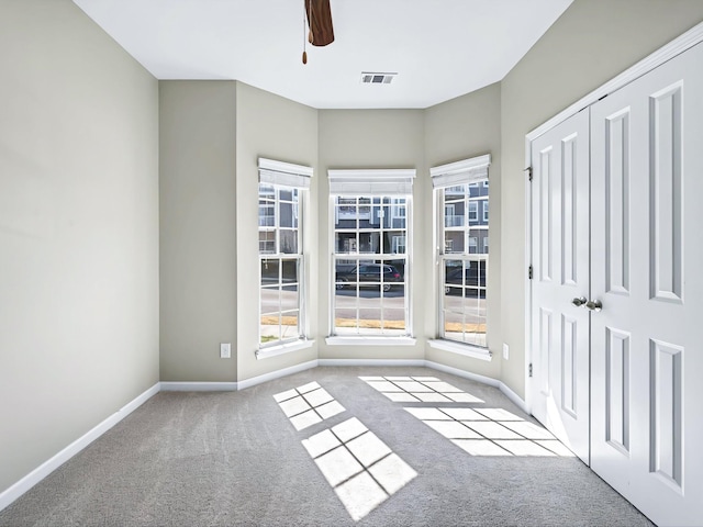 unfurnished room with carpet floors, visible vents, baseboards, and a ceiling fan